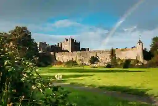 Stone walls of Cahir Castle with a rainbow overhead and green lawns in County Tipperary.