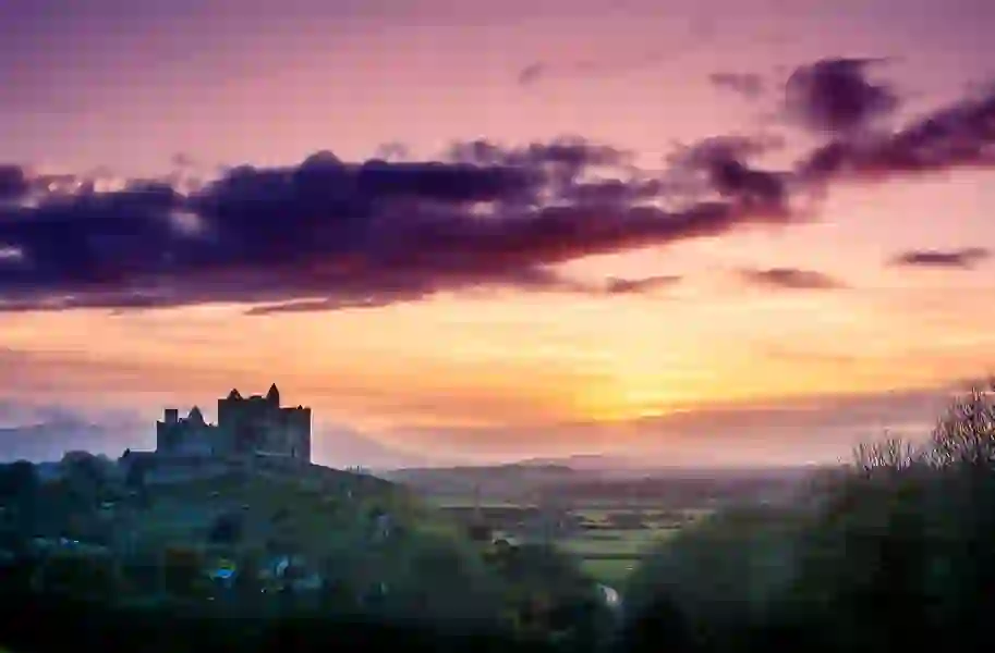 The Rock of Cashel silhouetted against a purple and orange sunset over County Tipperary.