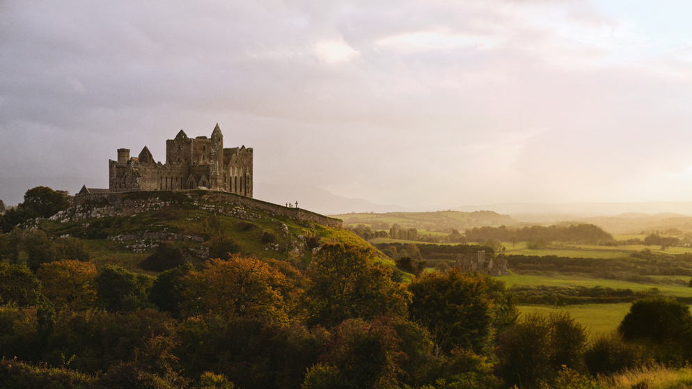 Rock of Cashel on a hill above County Tipperary countryside beneath dramatic sunbeams breaking through clouds.