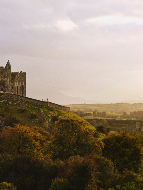 Rock of Cashel on a hill above County Tipperary countryside beneath dramatic sunbeams breaking through clouds.