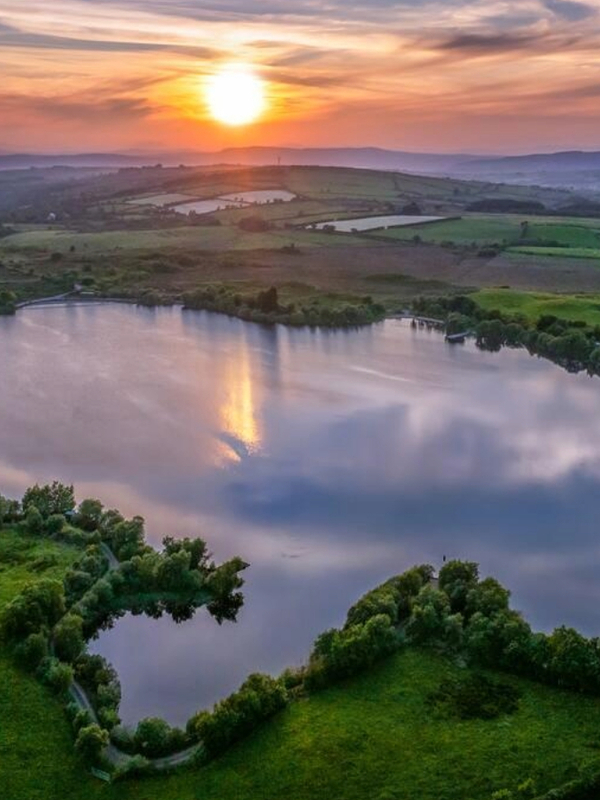 Sunset over Moorlough Lake, County Tyrone, reflected in calm water surrounded by green farmland.