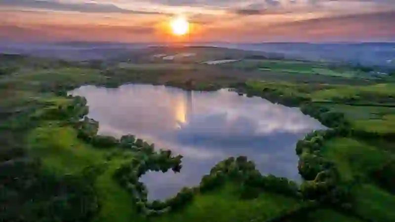 Sunset over Moorlough Lake, County Tyrone, reflected in calm water surrounded by green farmland.