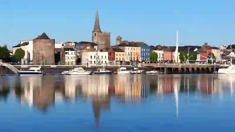 Waterford City skyline reflected on calm water with Reginald’s Tower, colourful buildings and marina views.