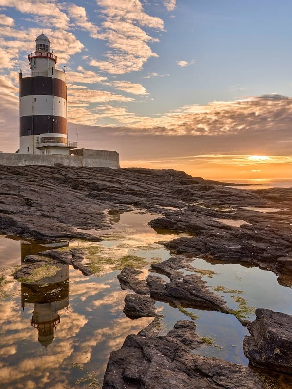 Le phare de Hook Head dans le comté de Waterford se reflète dans des mares résiduelles rocheuses à la tombée de la nuit, sous un ciel spectaculaire.