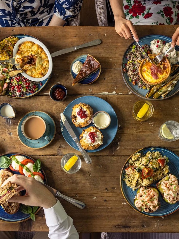 People enjoying brunch and coffee around a table filled with colourful dishes and desserts in Mount Congreve Gardens, County Waterford.
