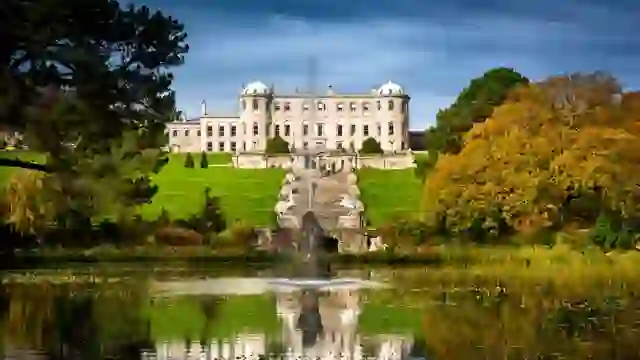 Powerscourt House overlooks formal gardens, a fountain and reflective lake framed by autumn trees in County Wicklow.