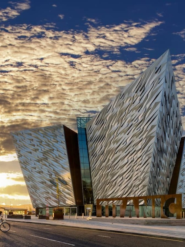 Titanic Belfast bij zonsondergang, met fietsers die langs de waterkant in het Titanic Quarter van Belfast rijden.