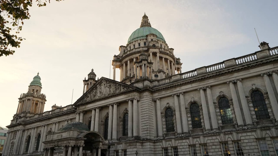 Das Rathaus von Belfast im Stadtzentrum, stimmungsvoll in der Abenddämmerung beleuchtet, mit seiner beeindruckenden Kuppel und neoklassischen Architektur.