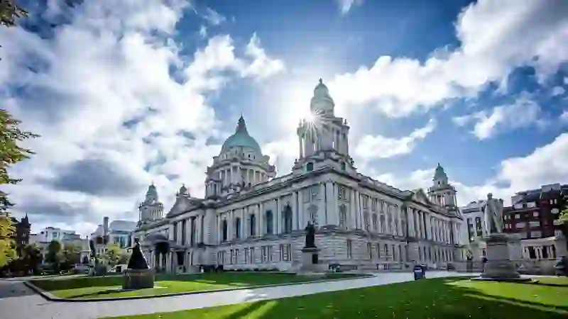 Belfast City Hall with its green domes and statues, lit by bright sunlight and blue skies.