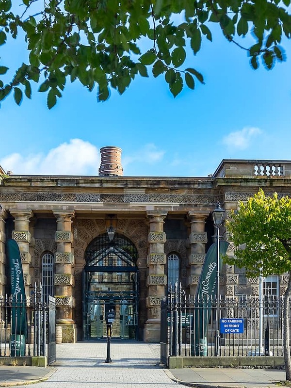 Crumlin Road Gaol in Belfast, with its grand stone entrance and iron railings under blue skies.