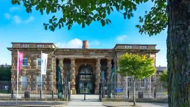 Crumlin Road Gaol in Belfast, with its grand stone entrance and iron railings under blue skies.