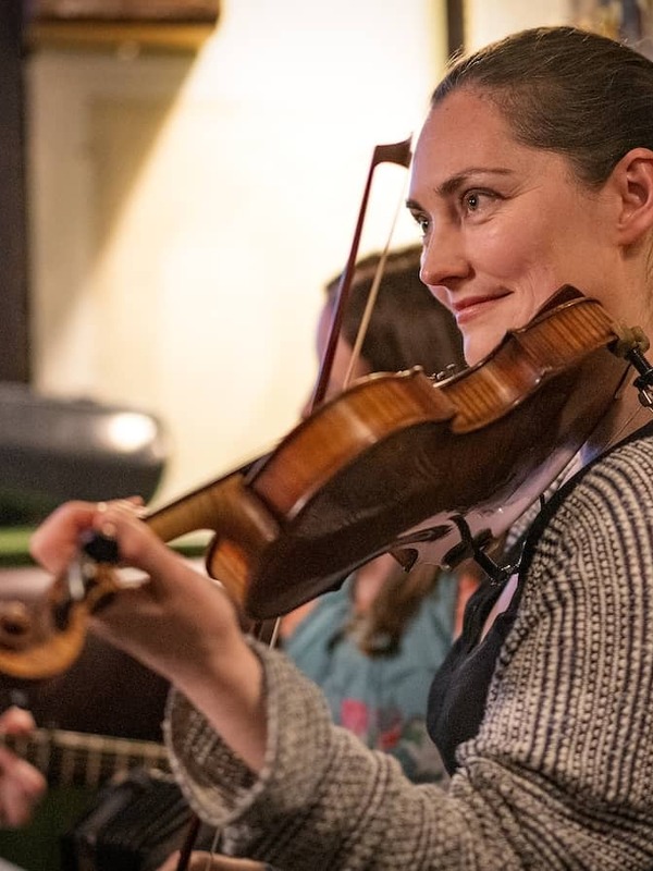 Traditional Irish music session in Belfast pub with fiddle player and guitarist performing indoors.