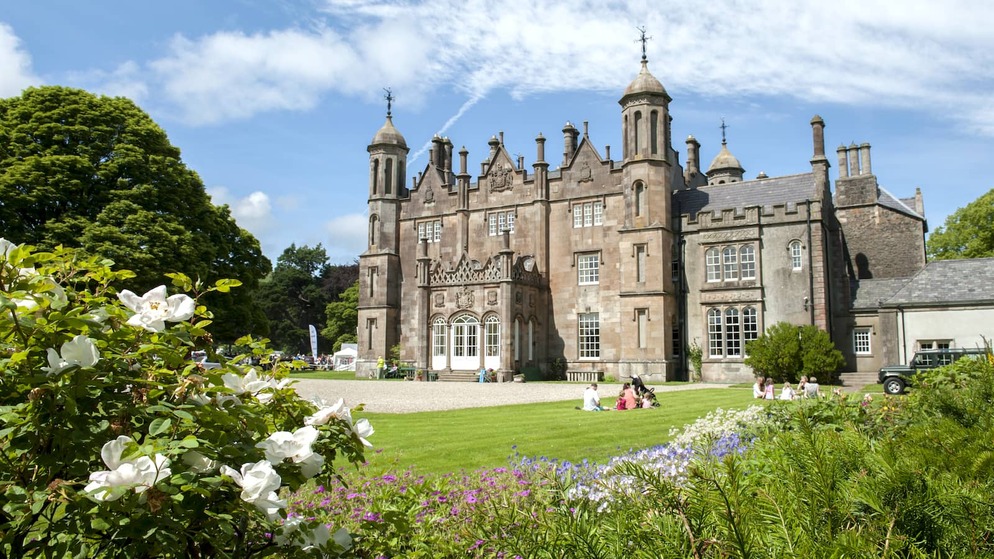 Glenarm Castle and gardens in County Antrim, with visitors relaxing on the lawn beside colourful flowerbeds.