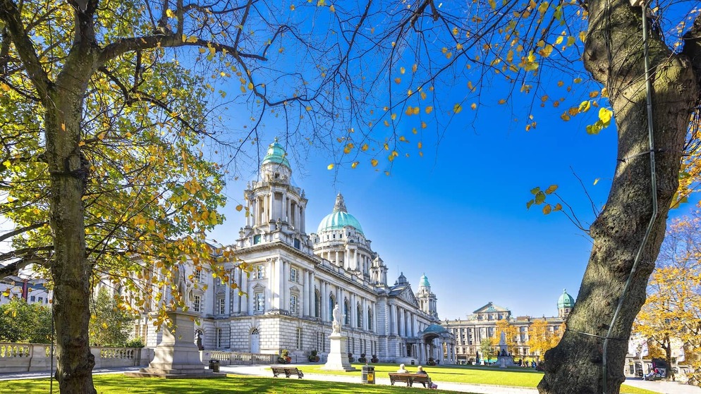 Belfast City Hall framed by autumn leaves, its green domes rising above the lawns and statues.