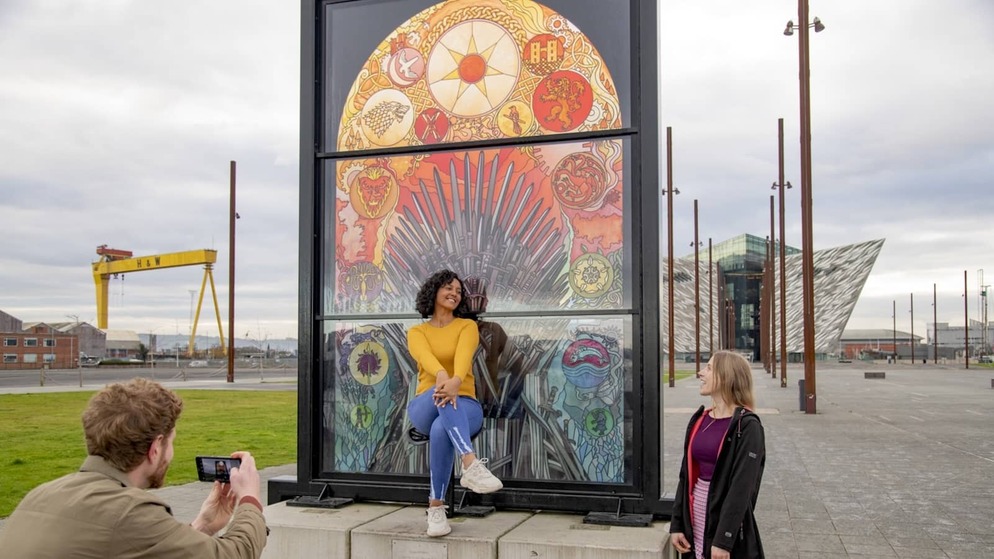 Friends posing beside the Glass of Thrones stained-glass artwork in Belfast’s Titanic Quarter.