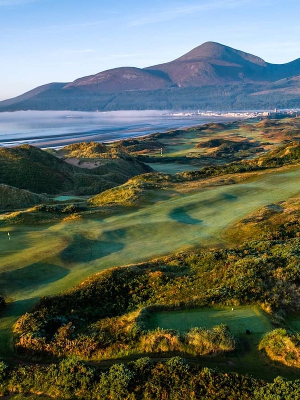 Royal County Down golf course at sunrise, with rolling dunes, Newcastle beach and the Mourne Mountains beyond.