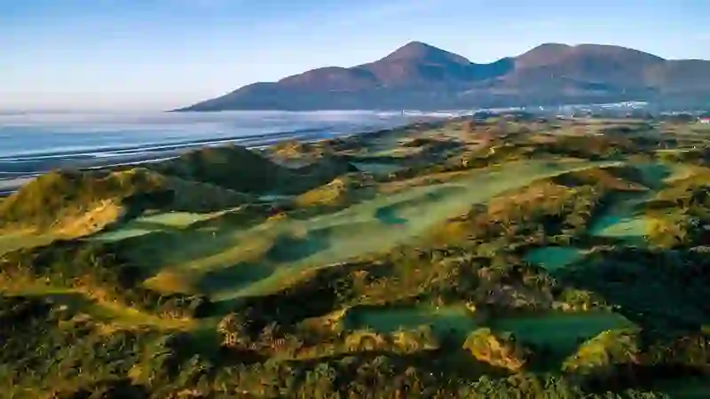 Royal County Down golf course at sunrise, with rolling dunes, Newcastle beach and the Mourne Mountains beyond.