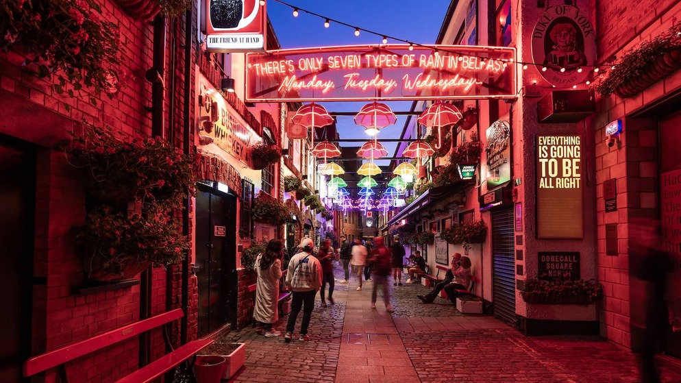 Commercial Court in Belfast at night, glowing with neon signs and colourful umbrella lights overhead.