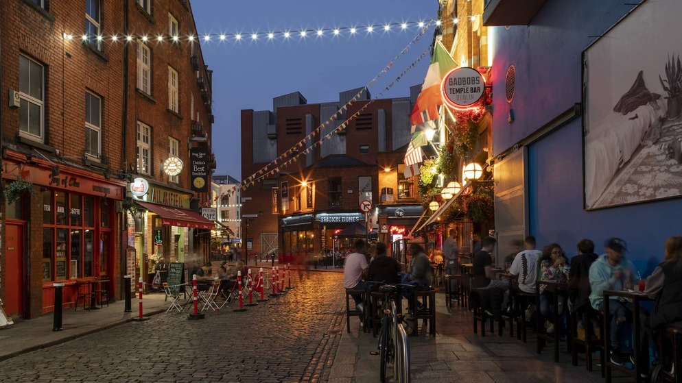 A lively evening street scene in Dublin’s Temple Bar with people dining outdoors under string lights.