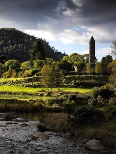 Ancient monastic ruins and round tower at Glendalough set against a backdrop of forested hills.