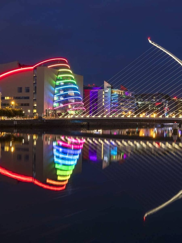 Kleurrijk verlicht Conventiecentrum en Samuel Beckett-brug weerspiegeld in de rivier de Liffey 's nachts.