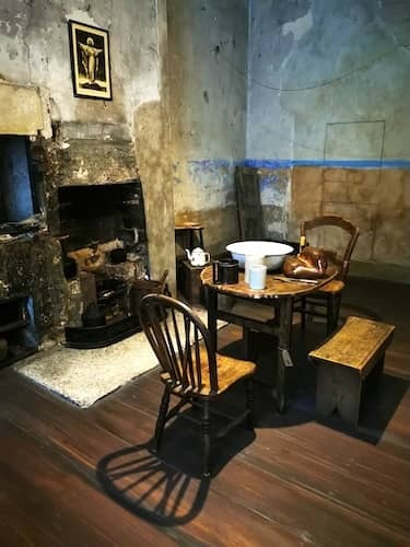 Interior of a historic tenement room with iron bed, wooden furniture, and an old fireplace in Dublin museum.