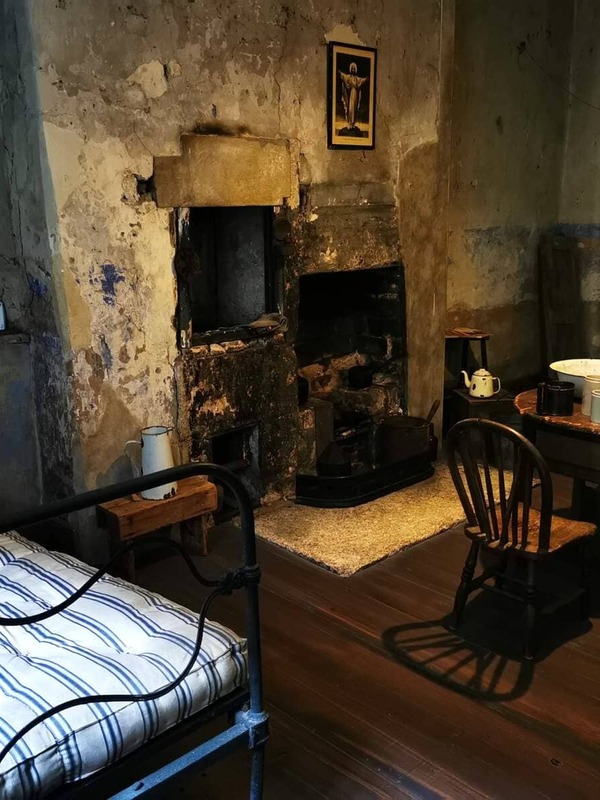 Interior of a historic tenement room with iron bed, wooden furniture, and an old fireplace in Dublin museum.