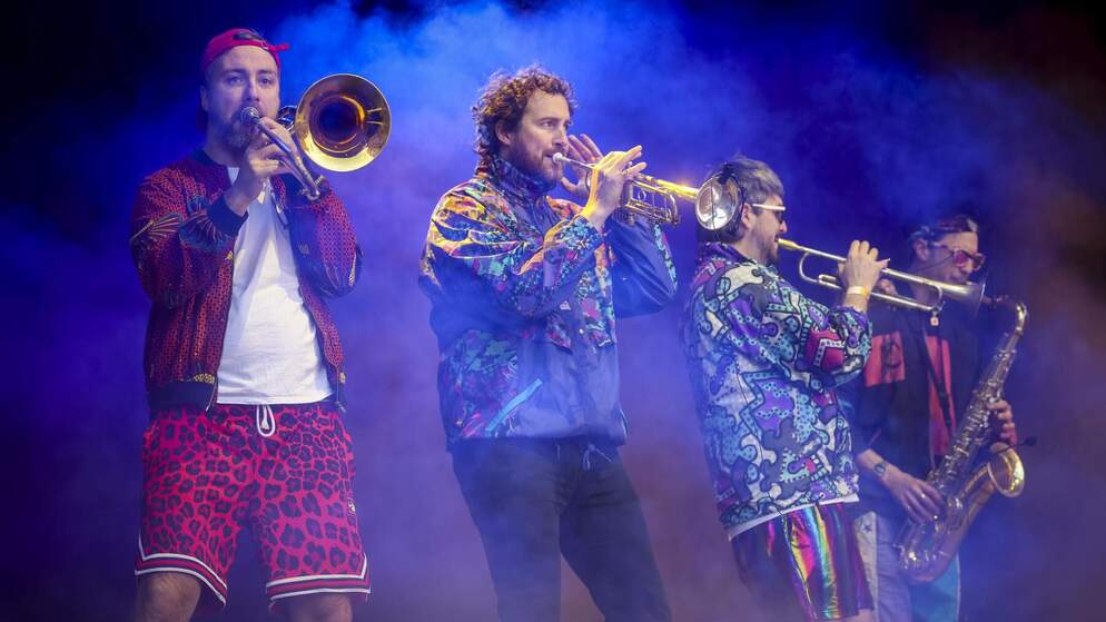 A brass band in colourful outfits during a live performance in Dublin, with energy and movement in the scene.