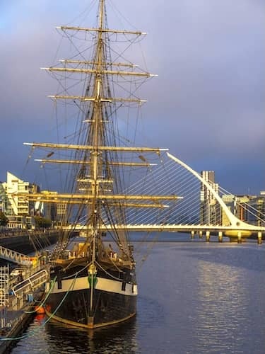 Tall ship moored on the River Liffey with Samuel Beckett Bridge and modern buildings in the background, Dublin.