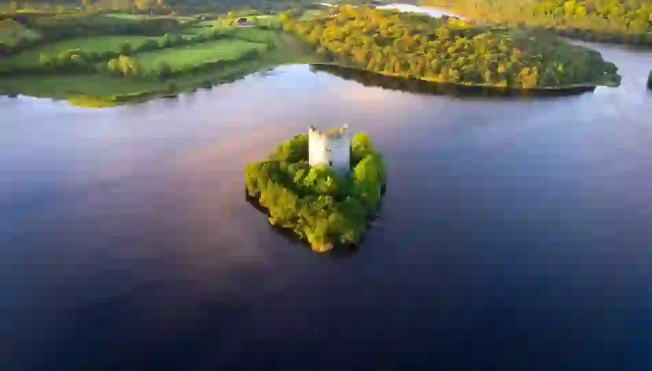 Aerial view of Cloughoughter Castle on a wooded island in Lough Oughter, County Cavan, surrounded by calm water.