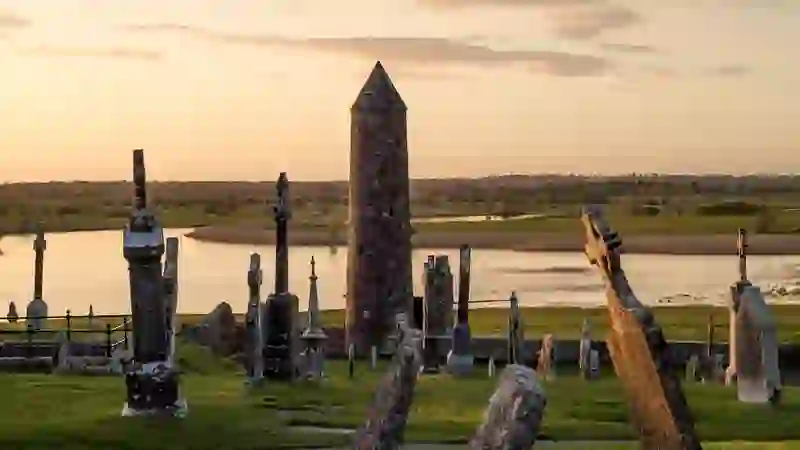 Clonmacnoise monastic site with round tower and gravestones overlooking the River Shannon at sunset in County Offaly.