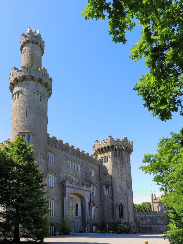 Charleville Castle, a striking neo-Gothic fortress in County Offaly, framed by lush green trees under a bright blue sky.