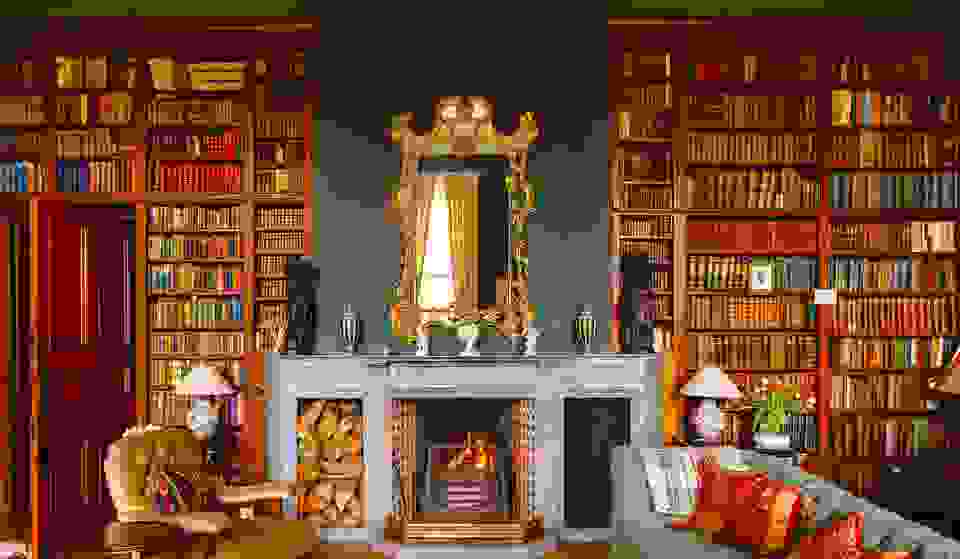 Elegant library at Clonalis House, County Roscommon, with tall wooden bookshelves, a marble fireplace, ornate mirror, and cosy fireside seating.