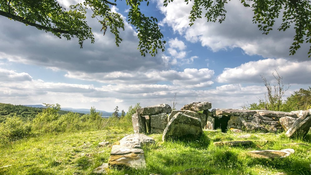 Prehistoric stone tomb surrounded by green grass and trees under a partly cloudy sky at Cavan Burren Park, County Cavan.
