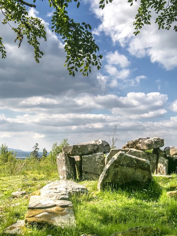 Prehistoric stone tomb surrounded by green grass and trees under a partly cloudy sky at Cavan Burren Park, County Cavan.