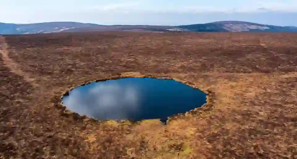 Aerial view of Clear Lake in the Slieve Bloom Mountains, County Offaly, a small circular lake surrounded by open peatland under a blue sky.