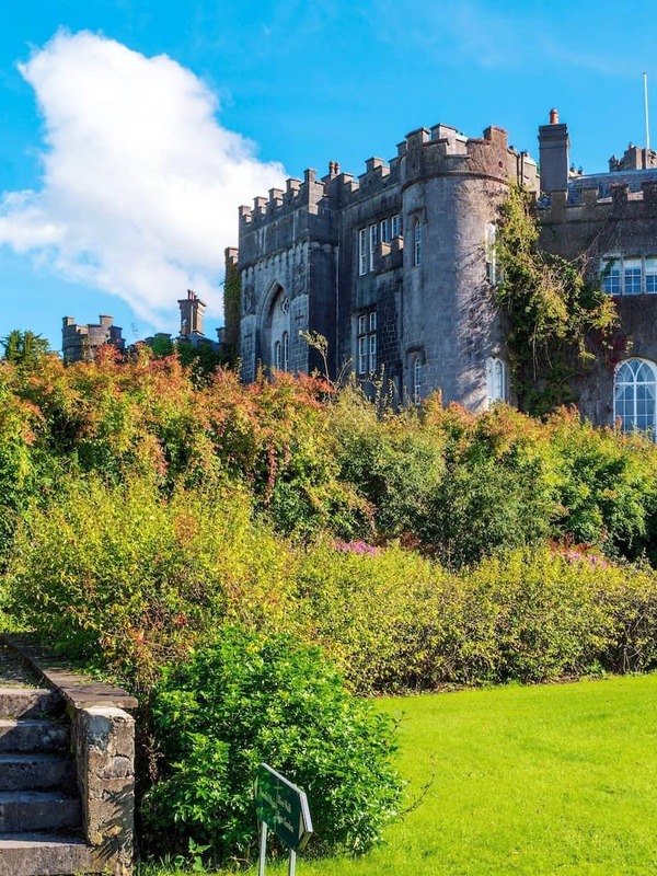 Birr Castle in County Offaly surrounded by lush gardens and greenery under a bright blue sky.