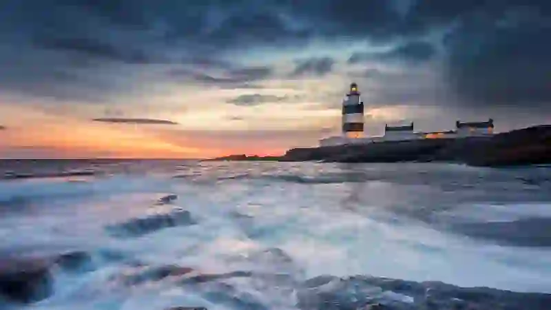 Hook Head Lighthouse standing on a rocky coastline of County Wexford as waves crash against the shore.