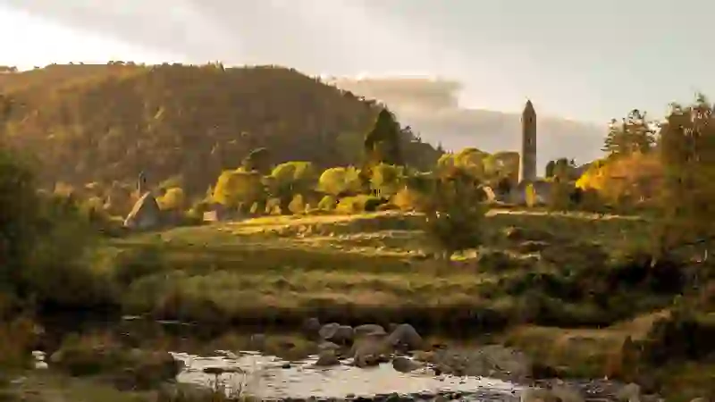 Round tower and monastic ruins at Glendalough, County Wicklow, set among wooded hills and a flowing stream.