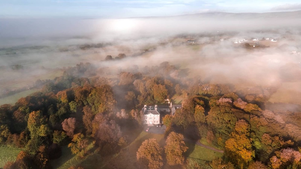 Aerial view of Roundwood House in County Laois, a grand country house surrounded by autumn woodland and misty countryside.
