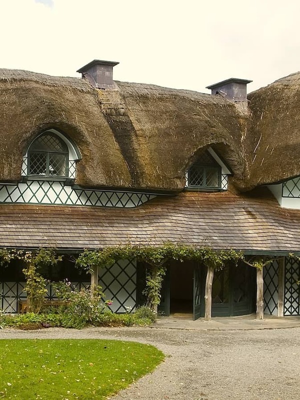 Traditional thatched Swiss Cottage in County Tipperary with timber detailing, surrounded by gardens and trees.