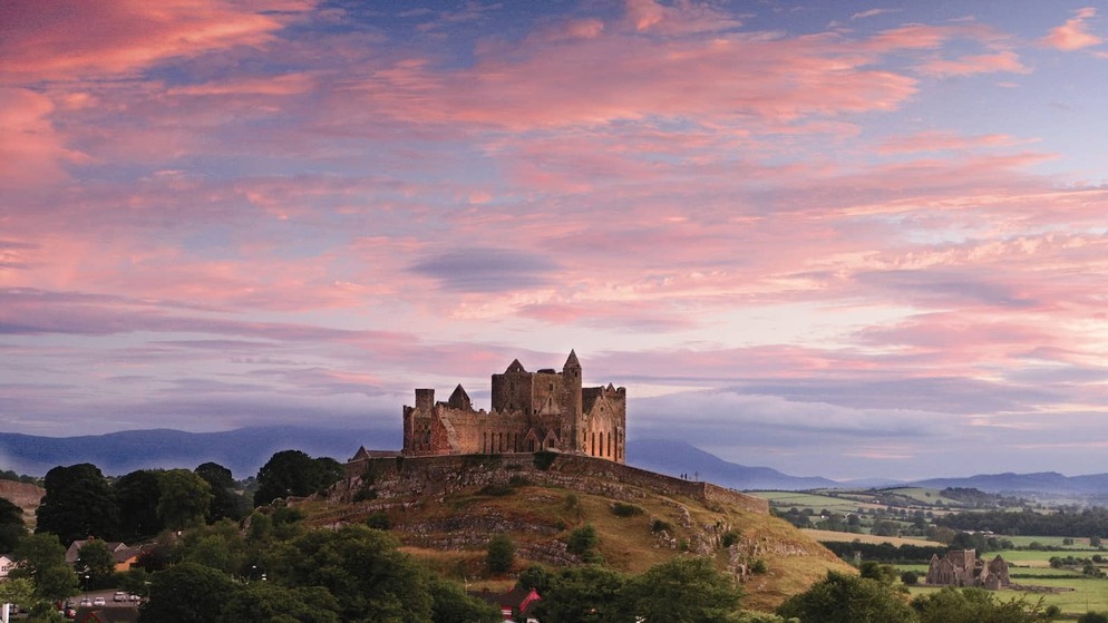 Rock of Cashel in County Tipperary, silhouetted on a hilltop above green countryside under a vivid pink and blue sunset sky.