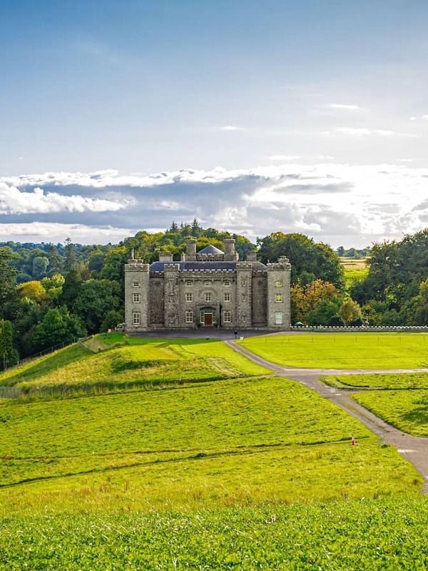 Slane Castle in County Meath, set on a grassy hillside with trees and countryside under a bright sky.