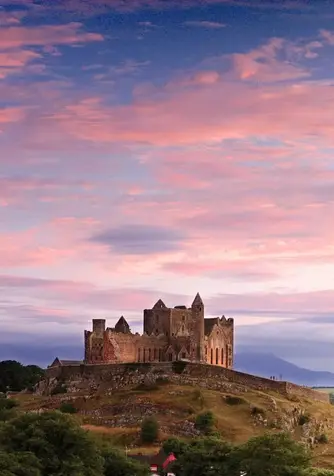 Rock of Cashel in County Tipperary, silhouetted on a hilltop above green countryside under a vivid pink and blue sunset sky.