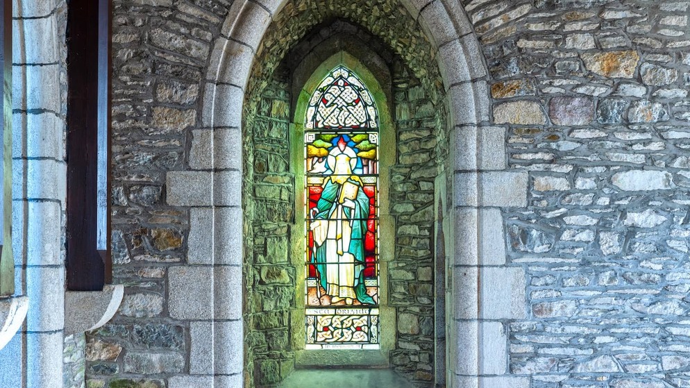 Stained-glass window in a stone archway at St Brigid’s Cathedral, Kildare, featuring a robed figure in vibrant colours.