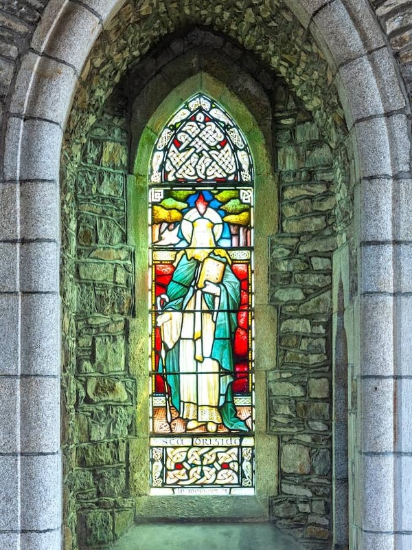 Stained-glass window in a stone archway at St Brigid’s Cathedral, Kildare, featuring a robed figure in vibrant colours.