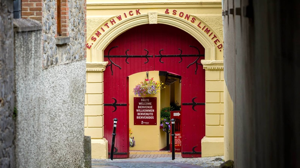 Red arched entrance to the Smithwick’s Experience in Kilkenny, with hanging flowers and a welcome sign inside.