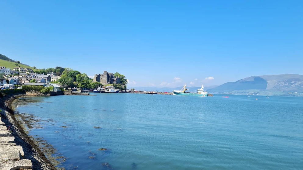 Coastal view of Carlingford, County Louth, with a harbour boat, castle ruins and mountains across Carlingford Lough.