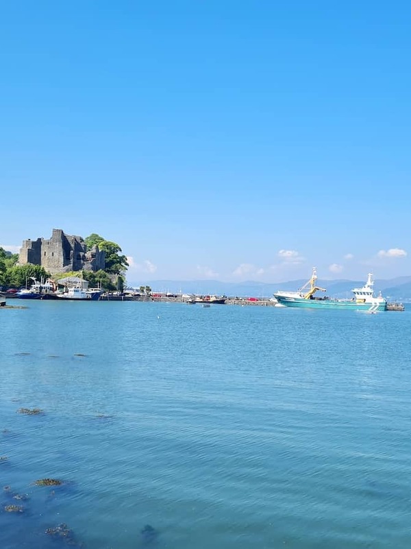 Coastal view of Carlingford, County Louth, with a harbour boat, castle ruins and mountains across Carlingford Lough.