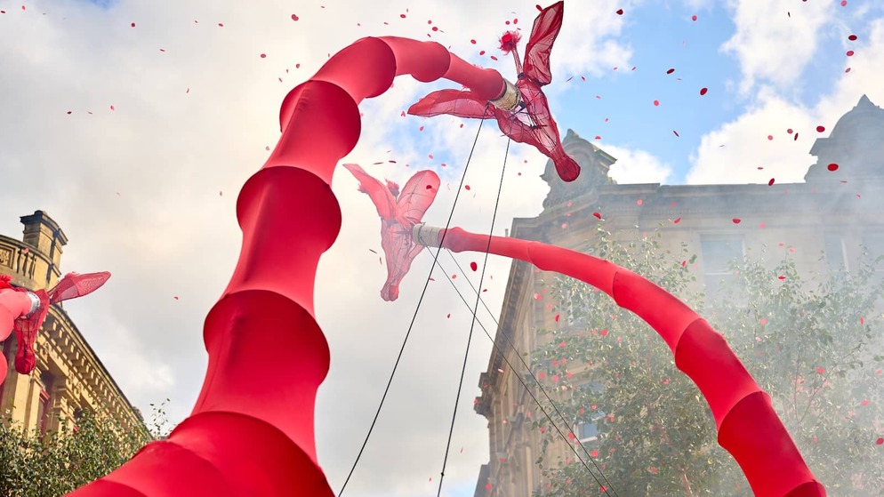Red stilt-walking performers towering above a city street, with confetti falling during a festival.